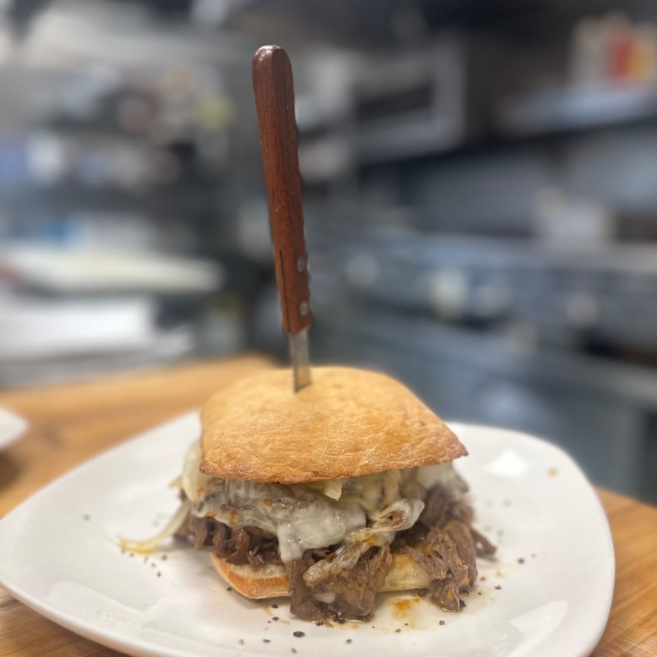 Amore Pizza and Pasta's Italian beef sandwich with melted cheese and onions, skewered with a knife.