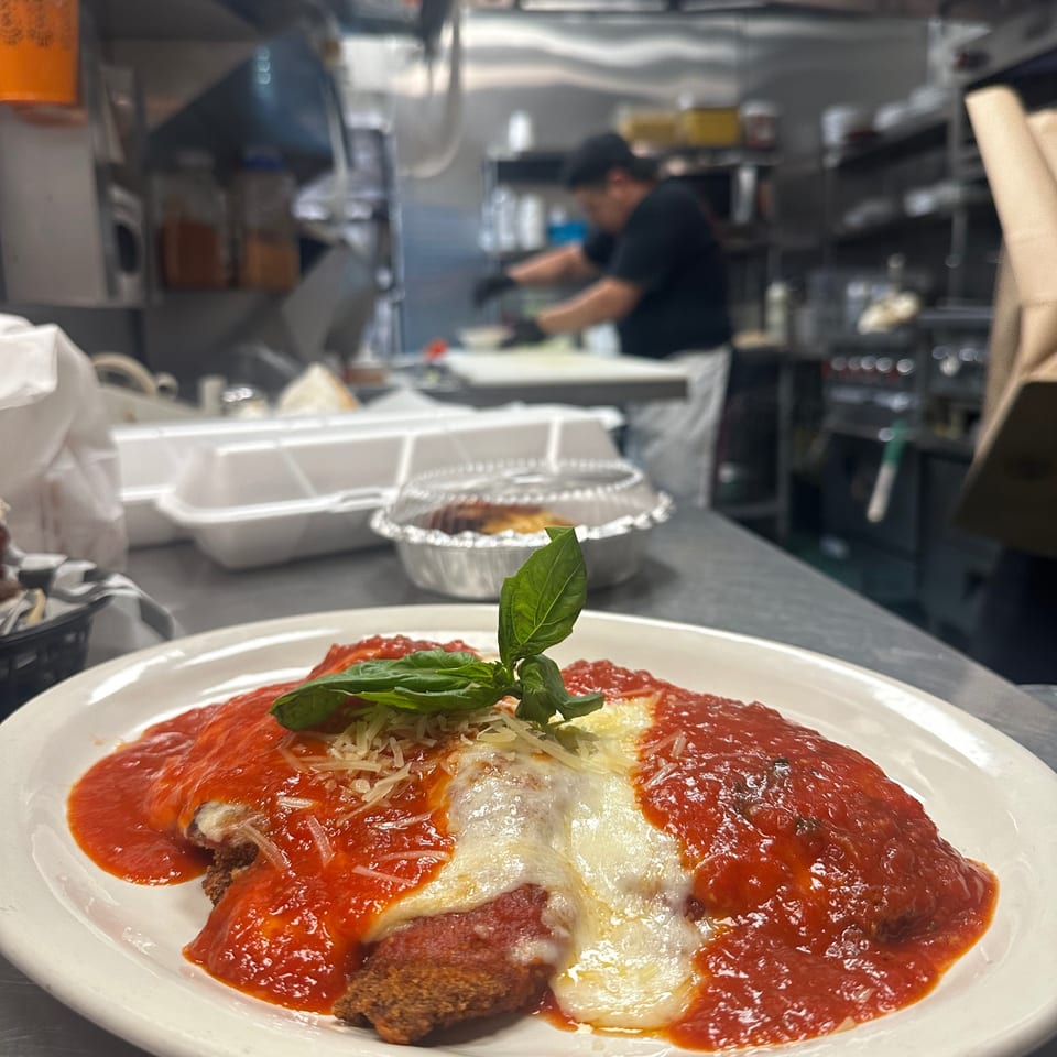 Chicken Parmesan with melted cheese, marinara sauce, and basil, in a busy kitchen.