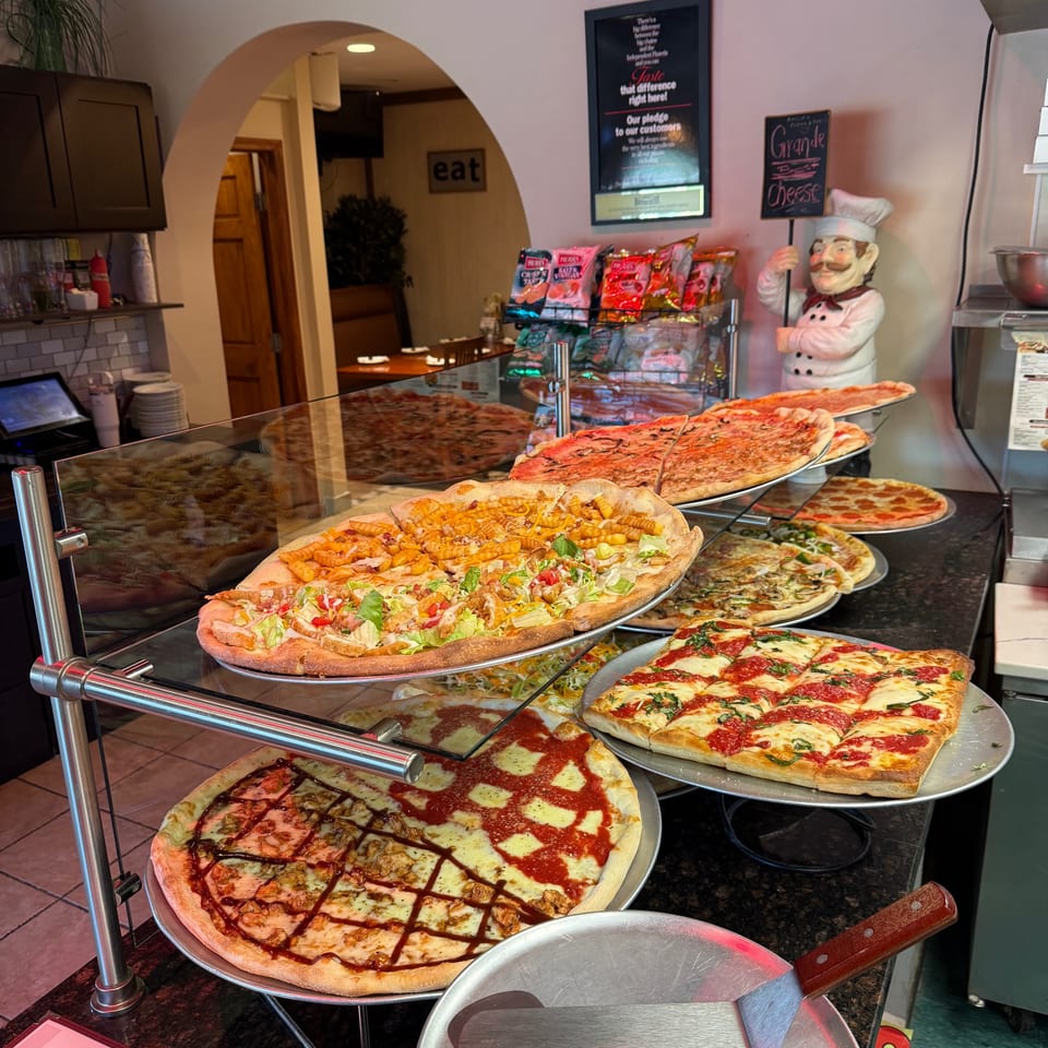 A variety of Amore Pizza and Pasta's specialty pizzas displayed on tiered racks in a brightly lit restaurant.
