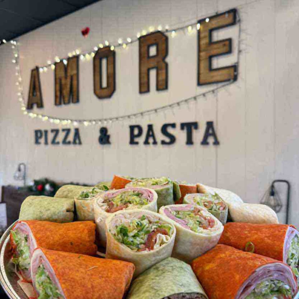 A platter of colorful wraps filled with meat and lettuce, in front of the Amore Pizza & Pasta sign.