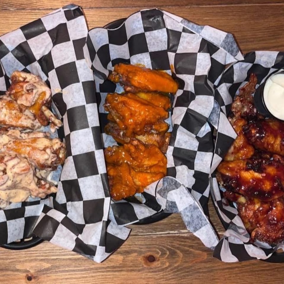 Three baskets of chicken wings, including garlic parmesan, buffalo, and BBQ, on a wooden table.