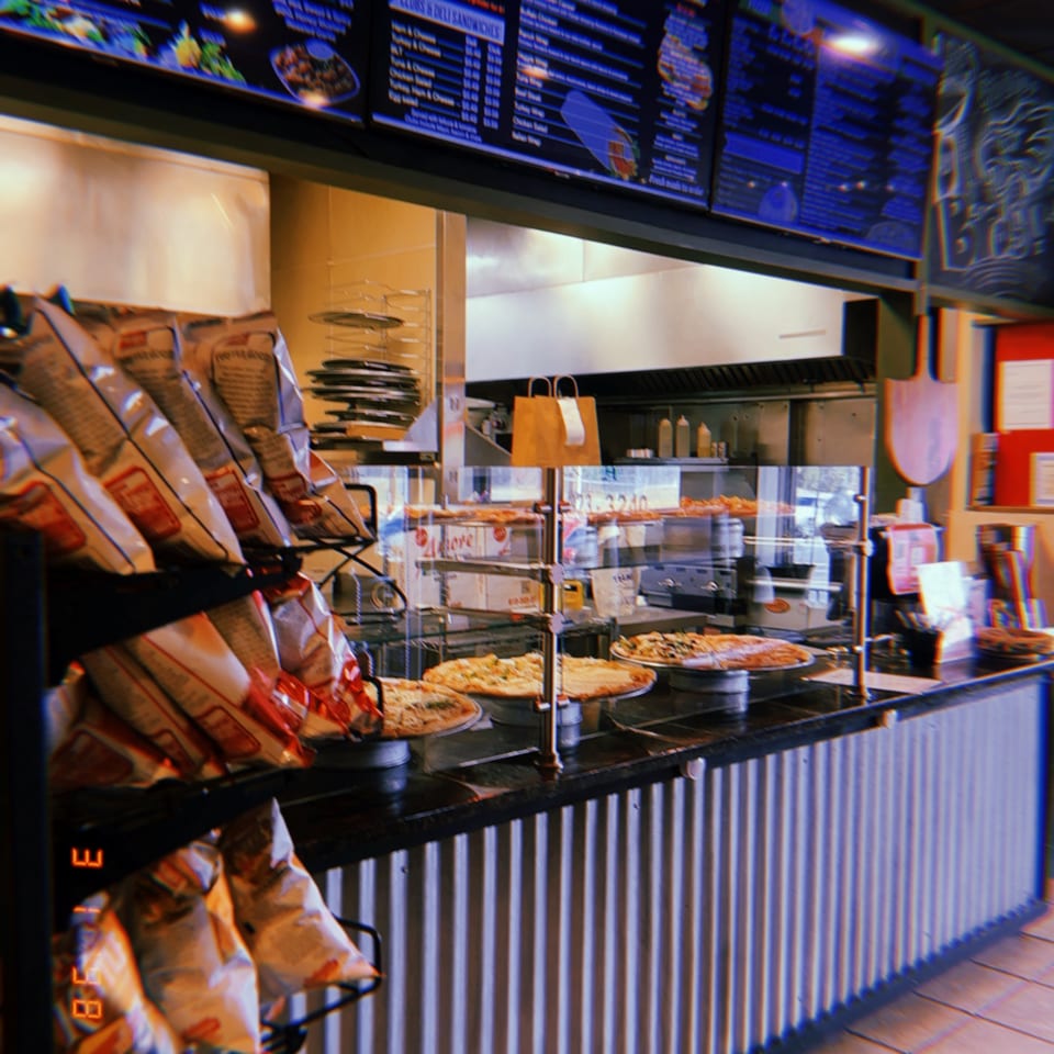 Amore Pizza and Pasta counter with various pizzas, chips, and a menu board.