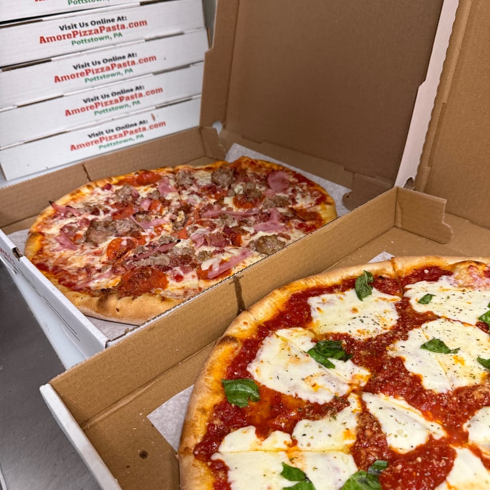 Two Amore Pizza and Pasta pizzas in open boxes, one with meat toppings, the other a Margherita.
